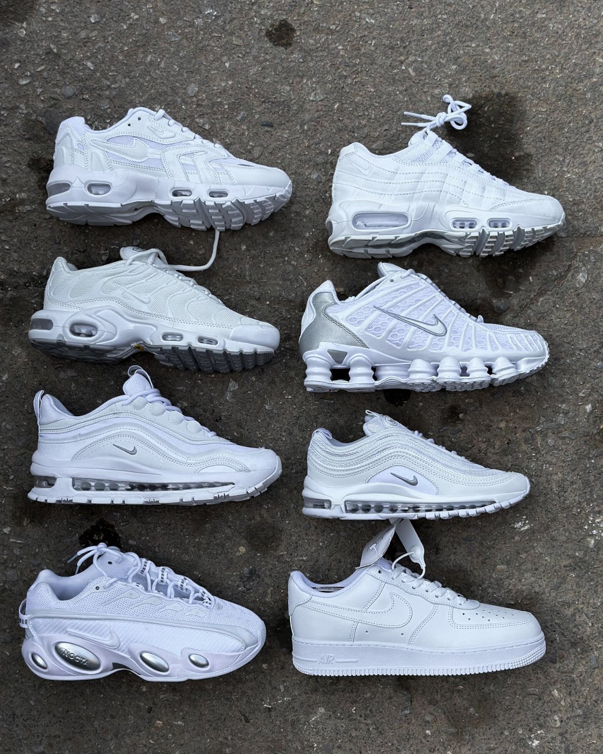 Eight pairs of all-white Nike sneakers arranged on a grey concrete surface.