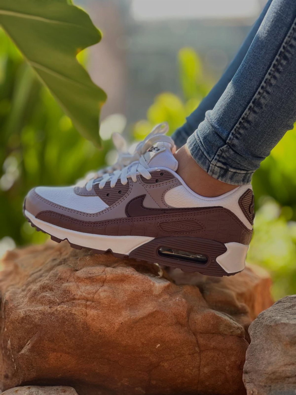 Beige and burgundy Nike sneakers with air cushioning worn with blue jeans.