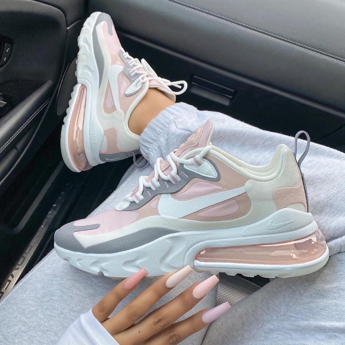 Beige and blush pink Nike sneakers with air cushioning worn with grey sweatpants.