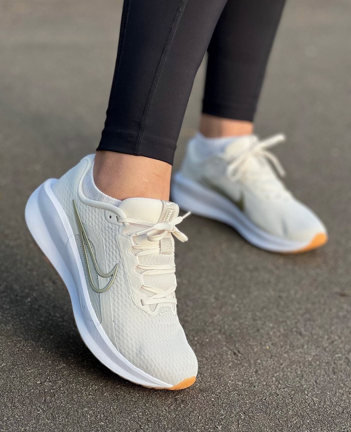 Beige Nike running shoes with white soles worn with black leggings on asphalt.
