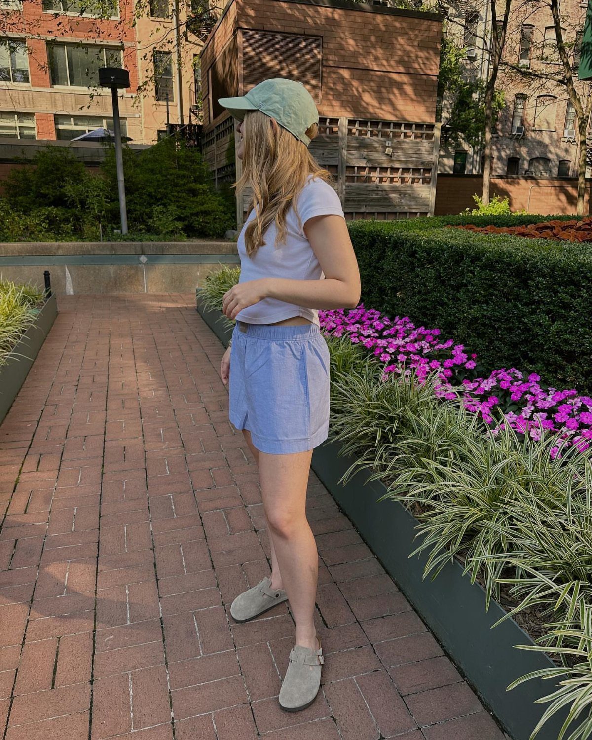 5 Birkenstock London Outfit Ideas, From Jeans to Blazers 3 Woman wearing light blue denim trouser shorts, white t-shirt, and grey clogs outdoors.