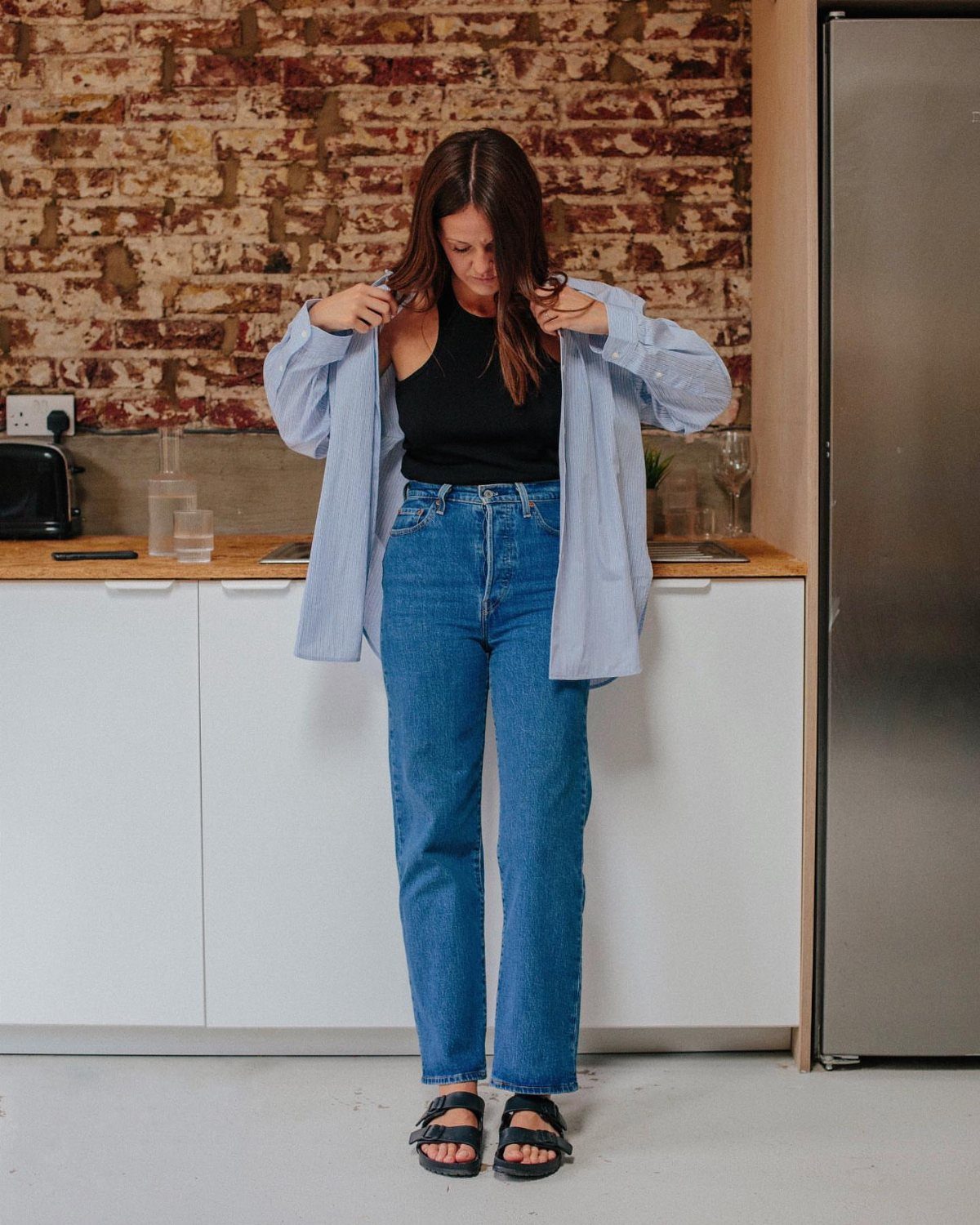 5 Birkenstock London Outfit Ideas, From Jeans to Blazers 1 Woman wearing a black vest top, straight-leg jeans, and black Birkenstock sandals.