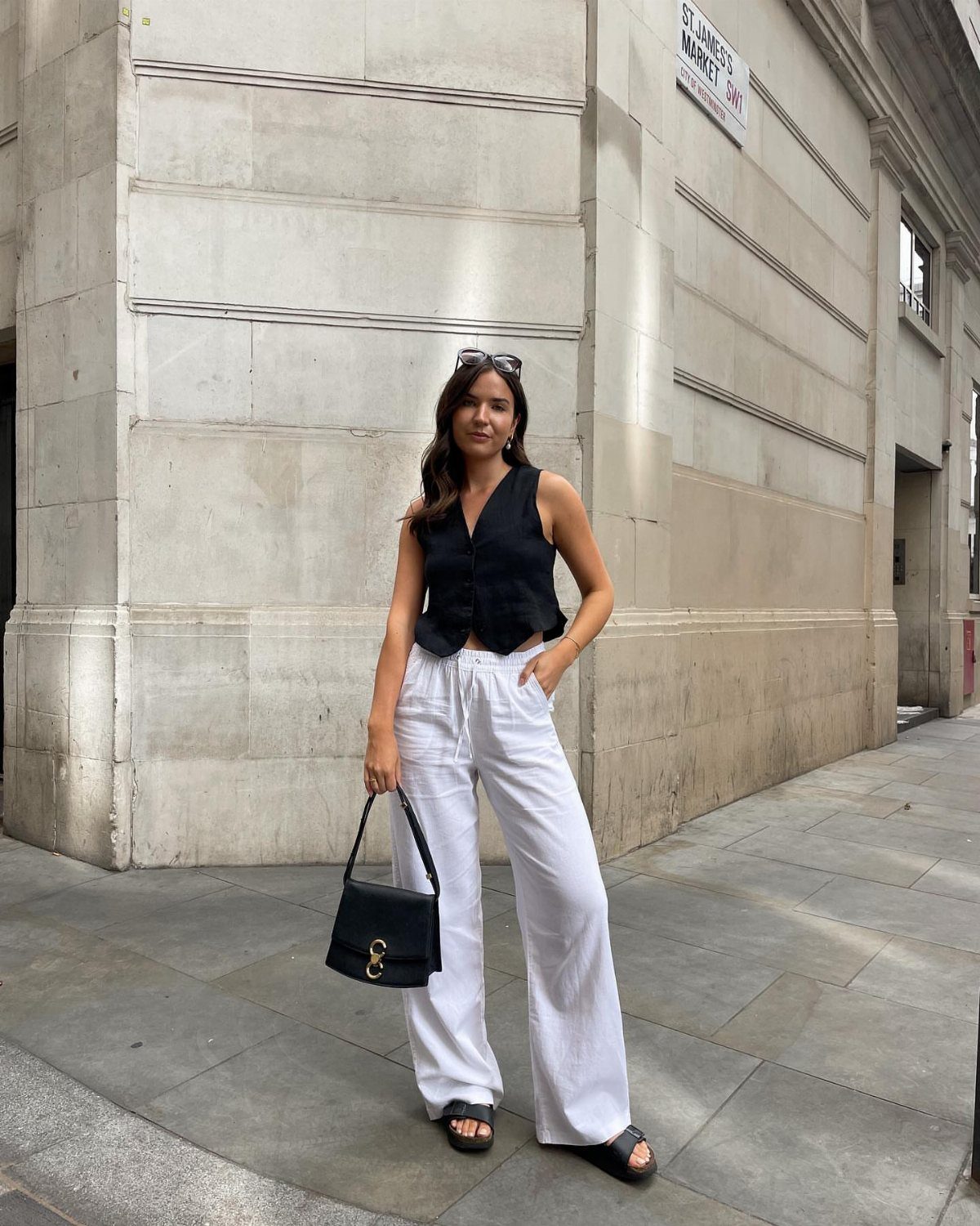 5 Birkenstock London Outfit Ideas, From Jeans to Blazers 2 Woman wearing a black vest top and white wide-leg trousers with black sandals.