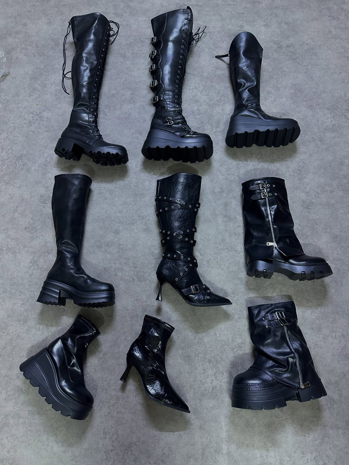 Nine black gothic boots of various heights and styles arranged on a grey background