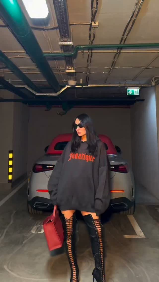 Woman in oversized black sweatshirt and lace-up thigh-high black boots in a garage