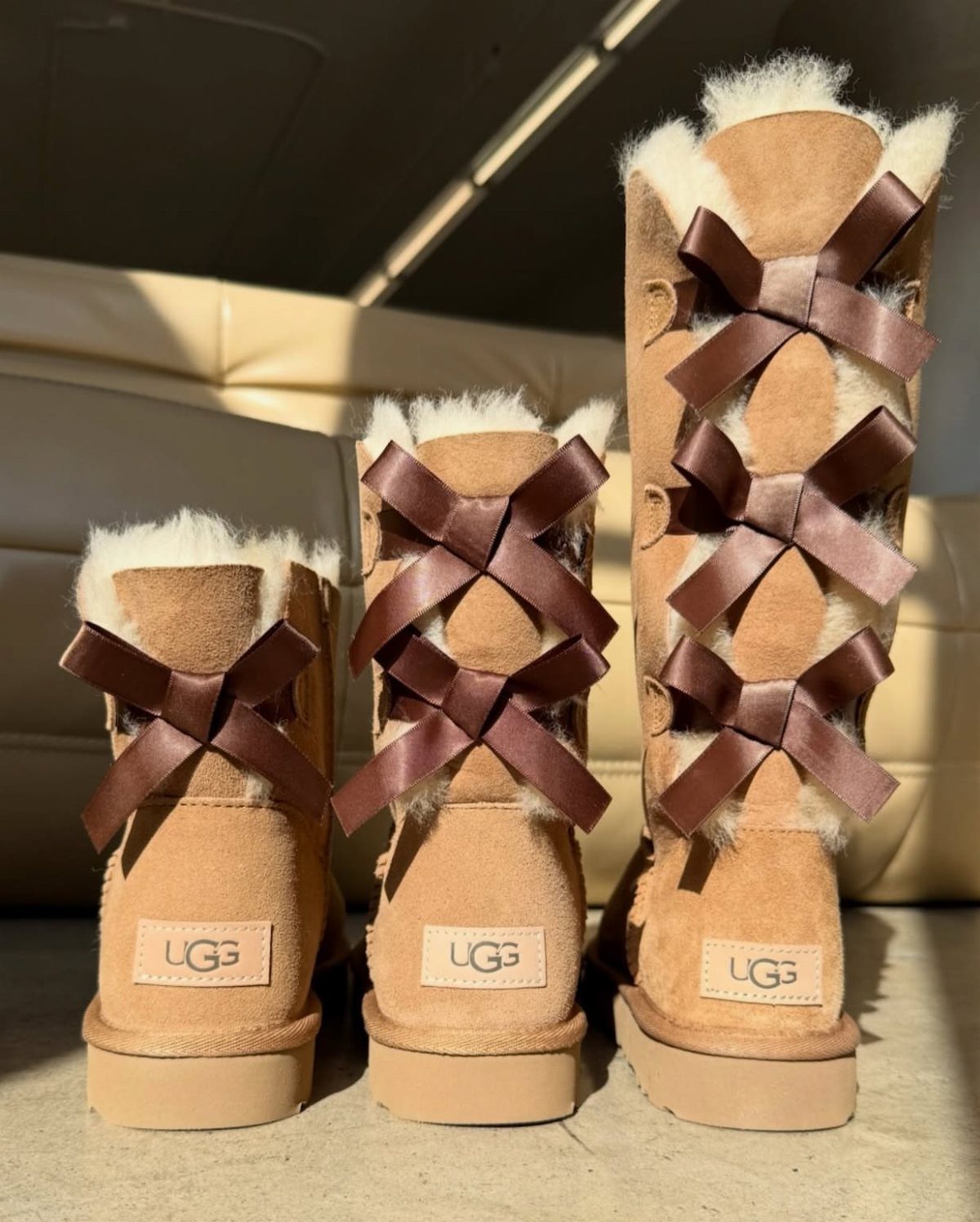 Tan suede UGG boots of varying heights decorated with brown satin ribbon bows.