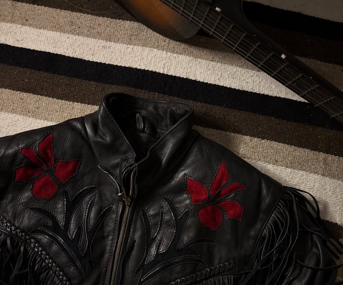 Black leather jacket with red floral embroidery and fringe on a striped rug.
