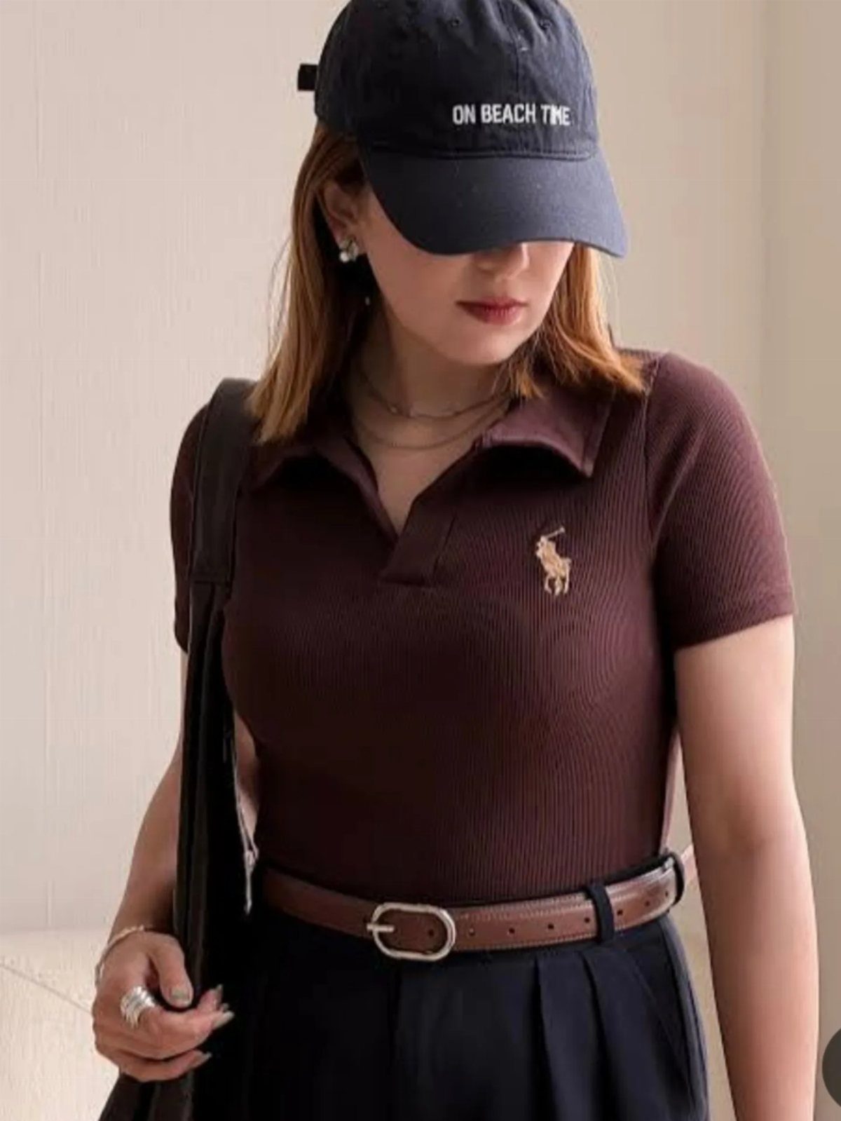Woman wearing a brown polo shirt, black cap, and black trousers with brown belt.