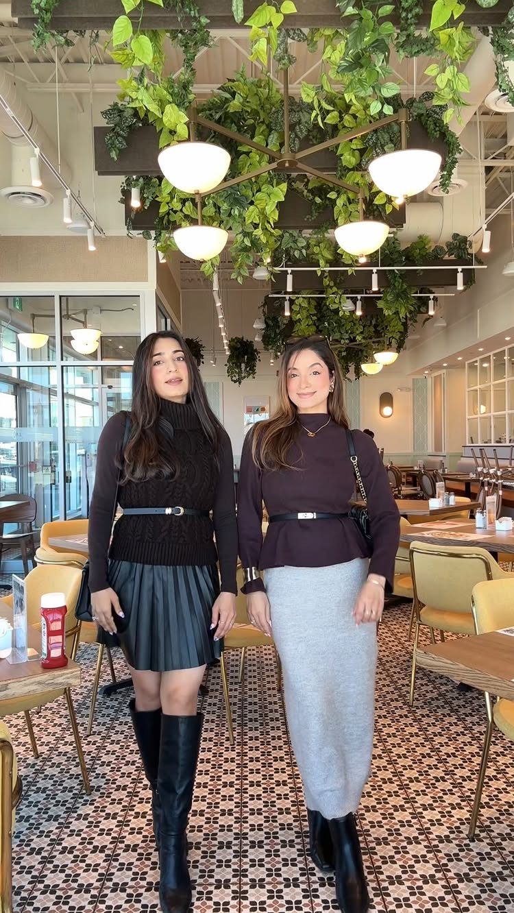 Two women posing in a restaurant wearing black boots and autumn outfits.