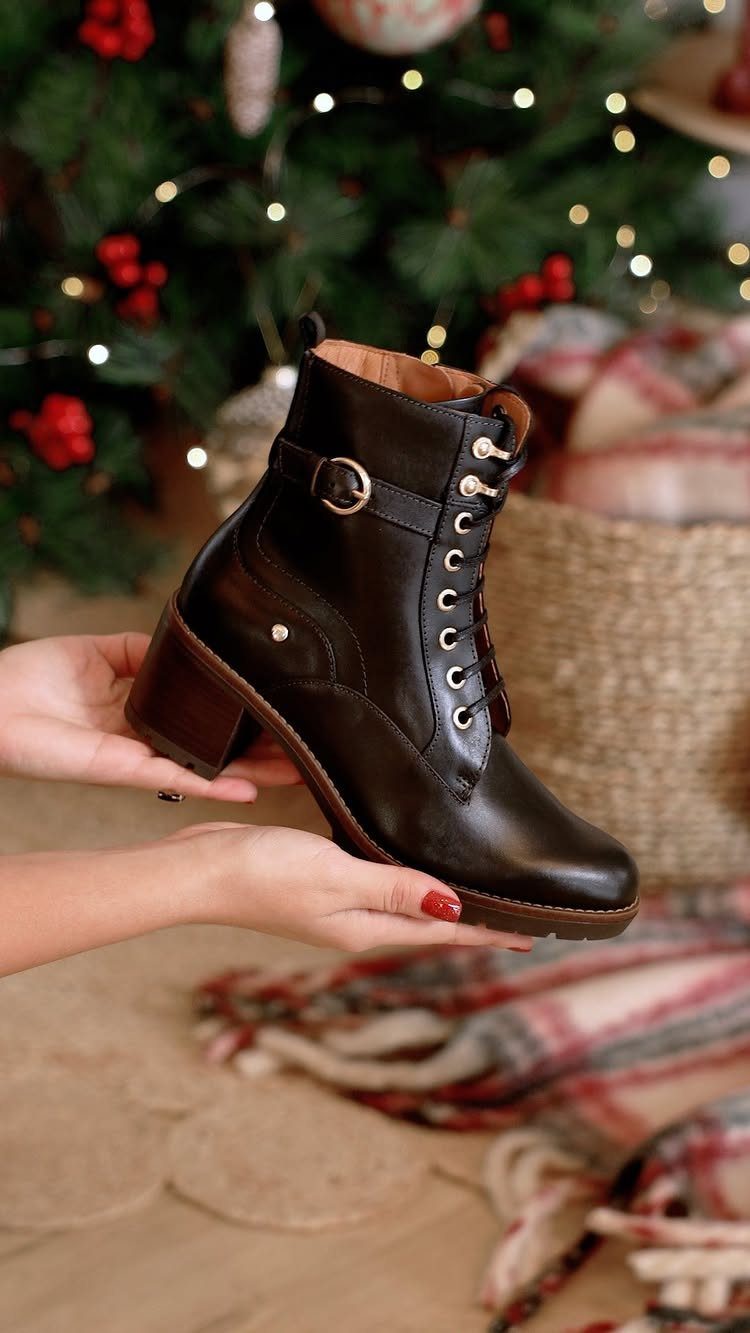 Dark brown leather buckle ankle boot held in hands before a Christmas tree.