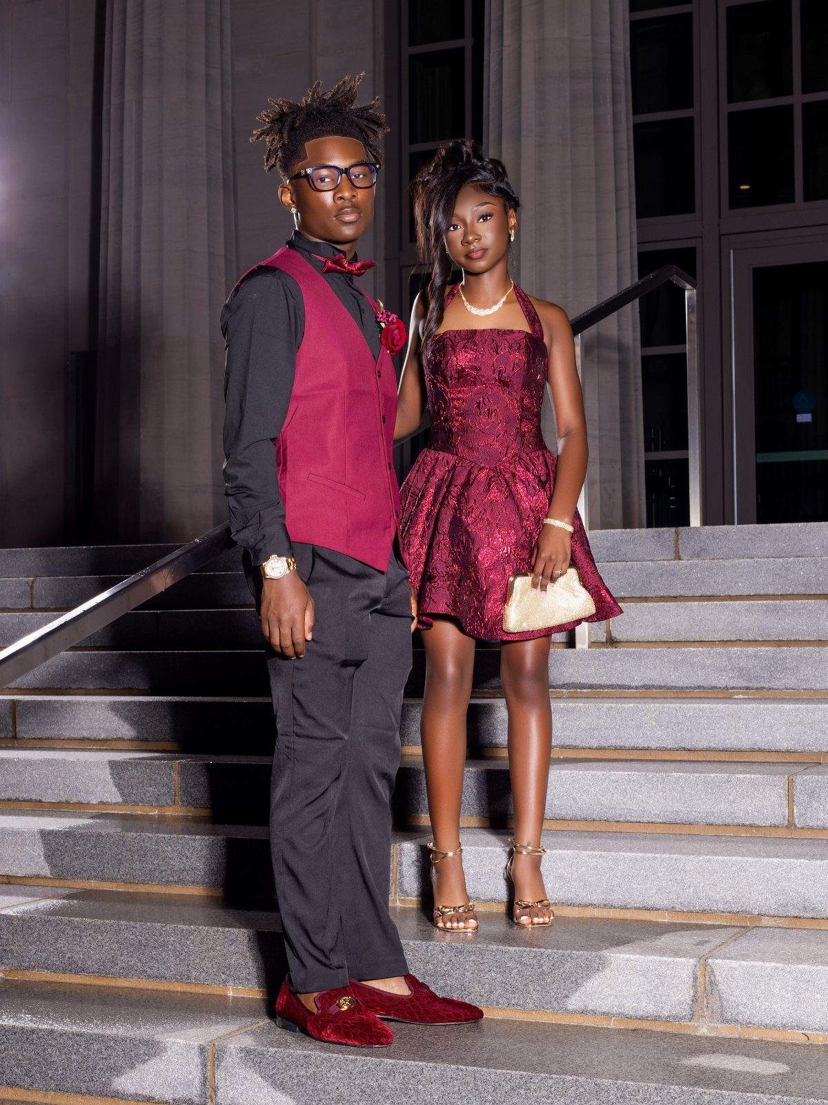 Couple posing on stairs, woman in sparkly burgundy dress and man in burgundy vest.