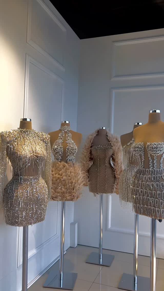 Four champagne-colored sequined and feathered short dresses displayed on mannequins in a studio.