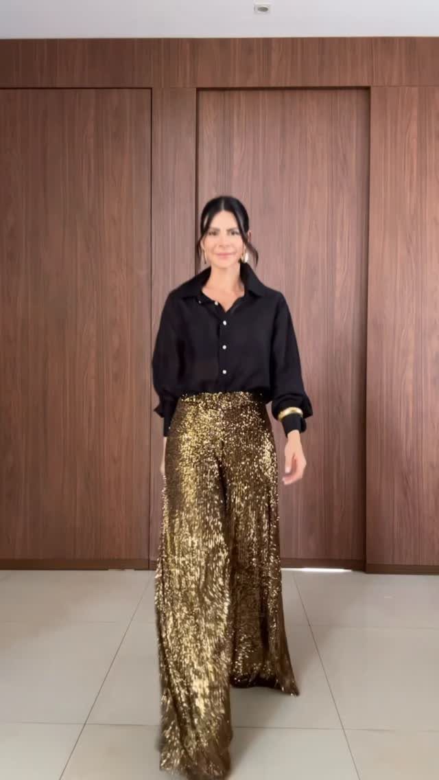 Woman wearing a black button-down shirt and gold sequin wide-leg trousers.