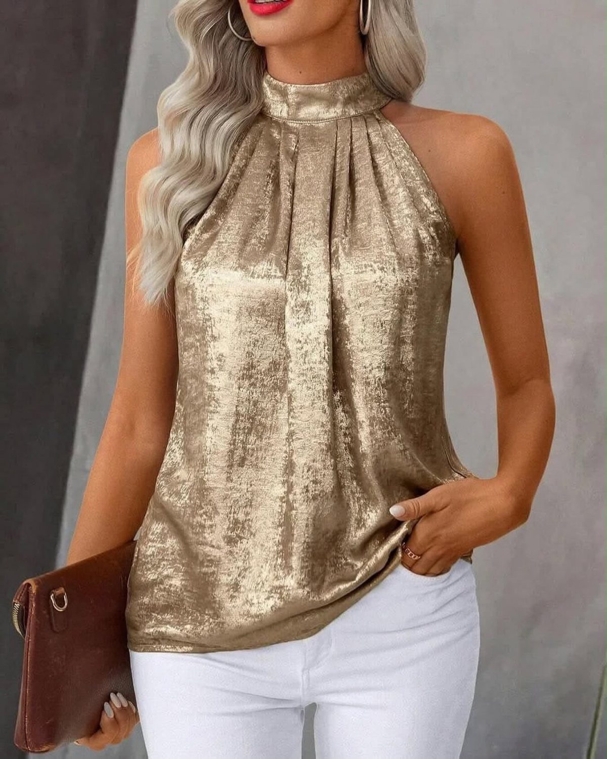 Woman wearing a metallic gold halter blouse and white pants with brown clutch.