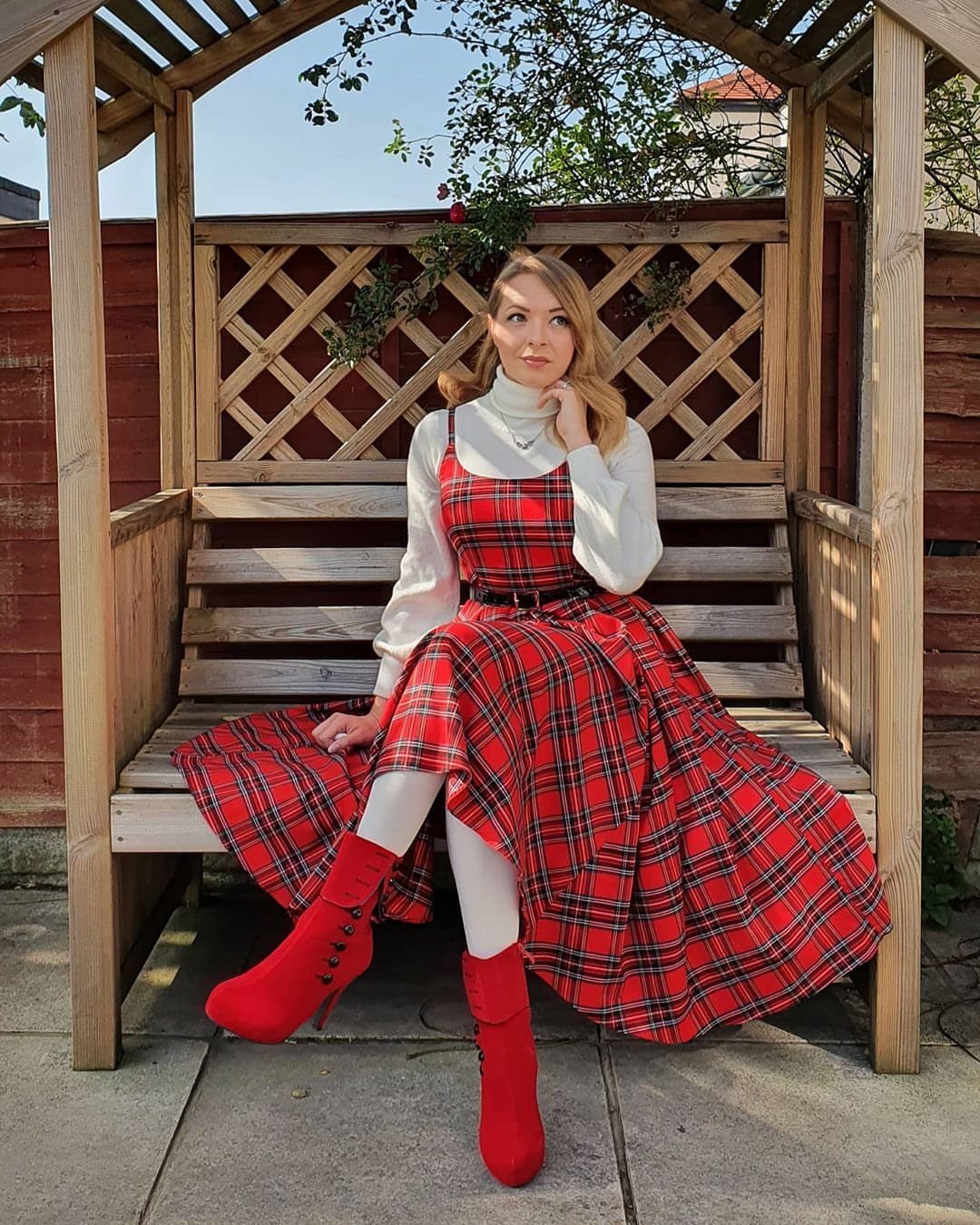 Woman wearing a red tartan plaid dress with white turtleneck and red boots.
