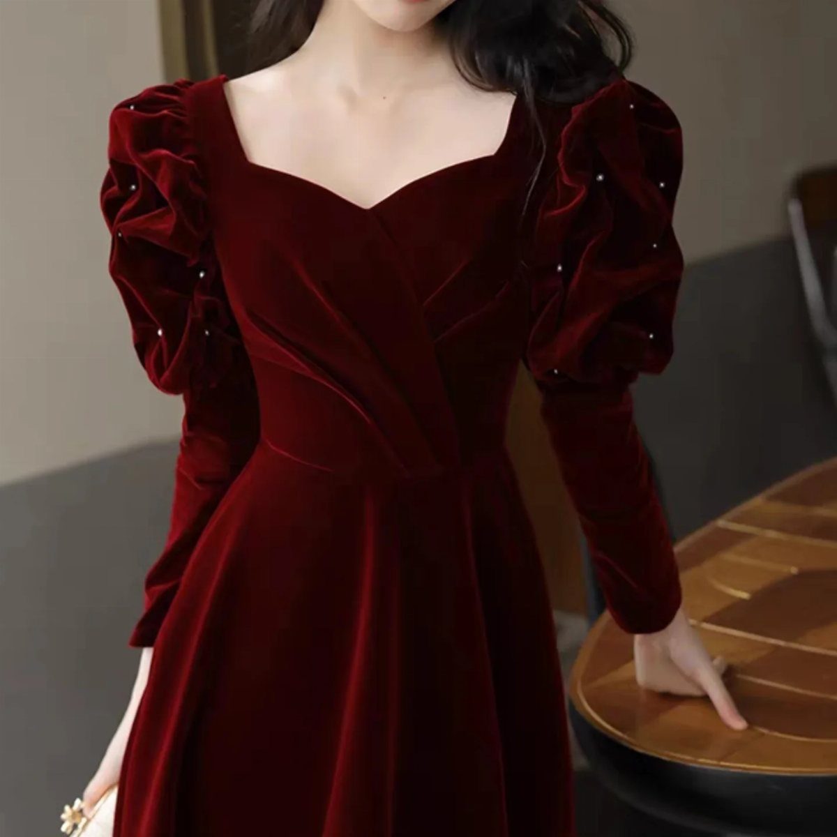 Woman wearing a deep red velvet dress with puffed pearl-detailed sleeves
