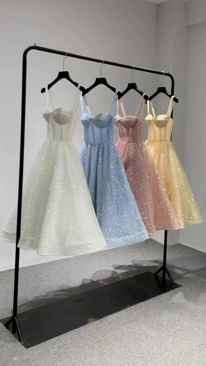 Four glittery A-line homecoming dresses in white, blue, pink, and yellow on a rack.