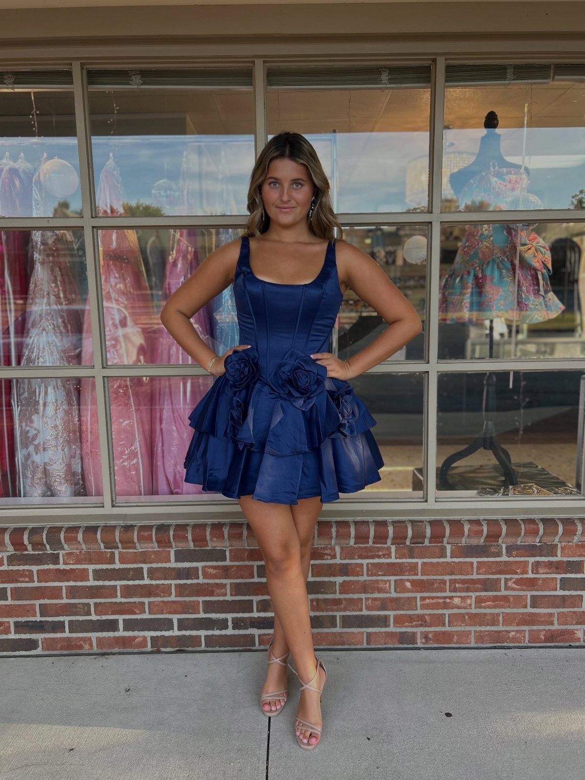 Young woman wearing a short navy blue satin homecoming dress with ruffled floral details.