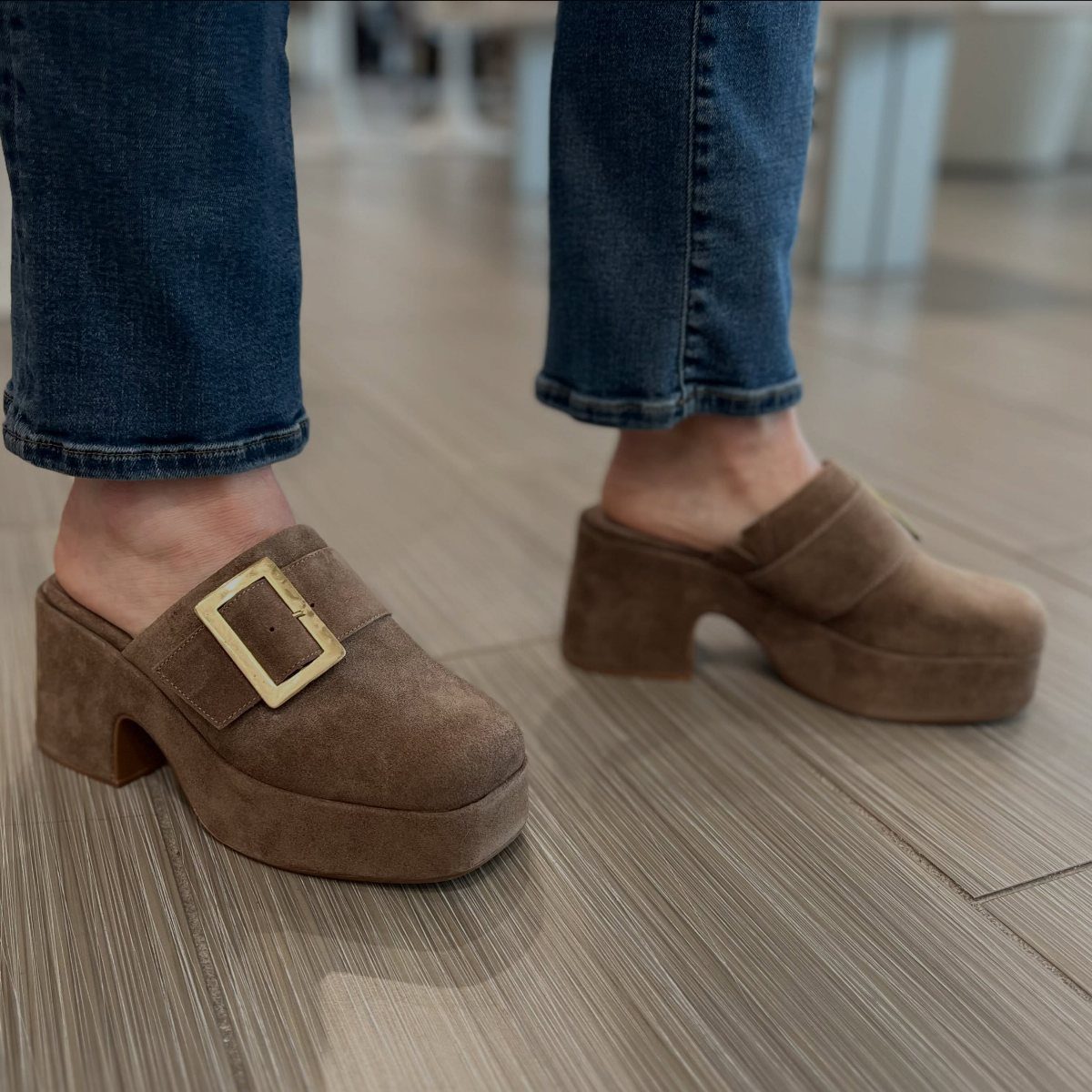 Brown suede platform heeled clogs with gold buckles worn with blue jeans.