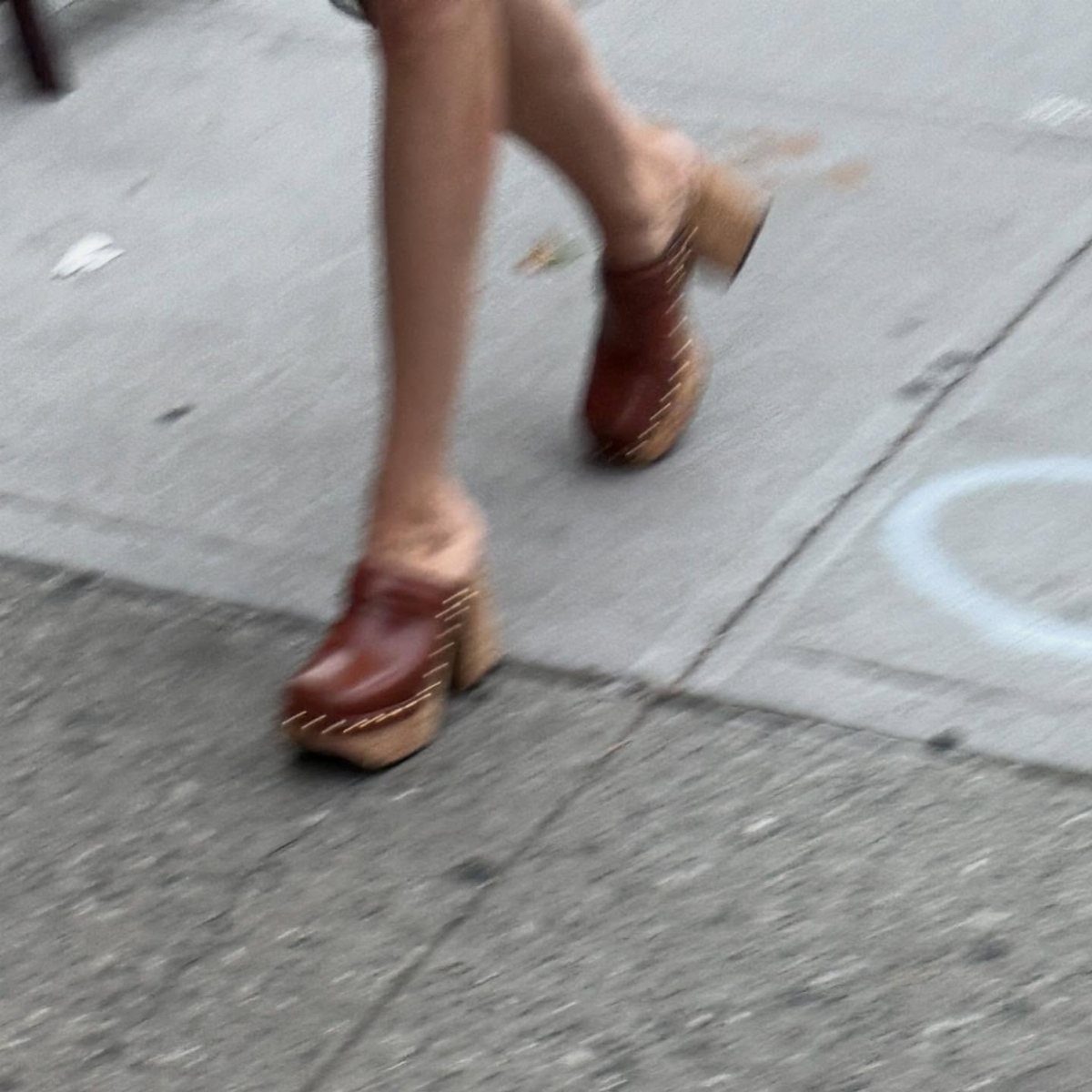 Brown leather heeled clogs with wooden soles worn by a person walking outdoors.