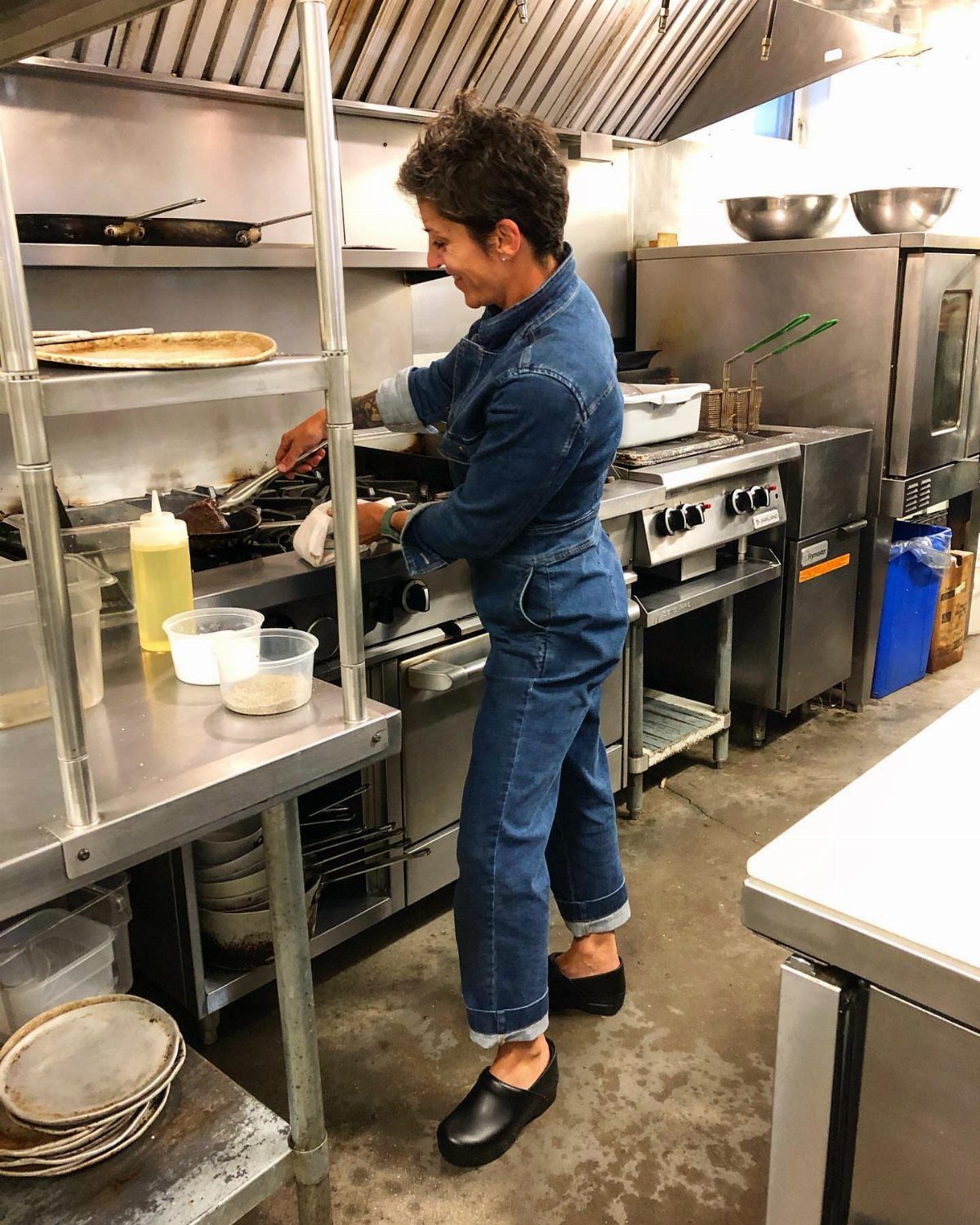 Woman in denim jumpsuit wearing black work clogs in a commercial kitchen