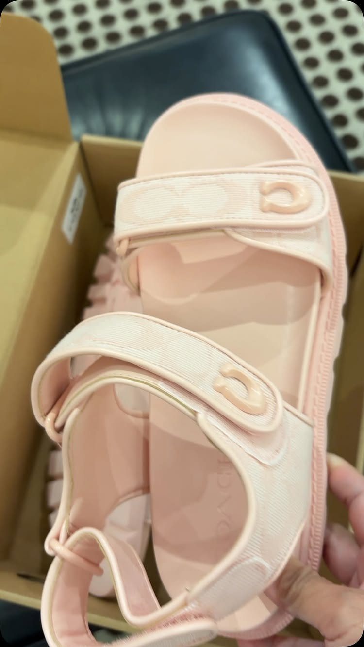 Light pink sandals with ankle straps and logo patterns inside a cardboard box
