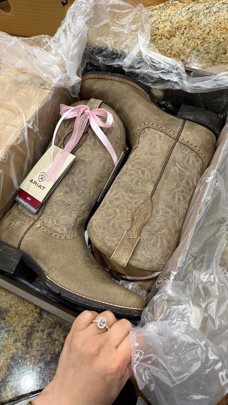 Tan Ariat cowgirl boots inside a shipping box with a brand tag attached.