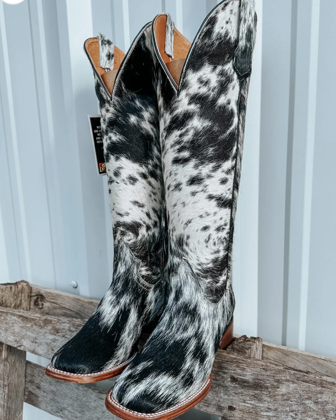 Black and white animal print cowgirl boots with square toes on wooden bench