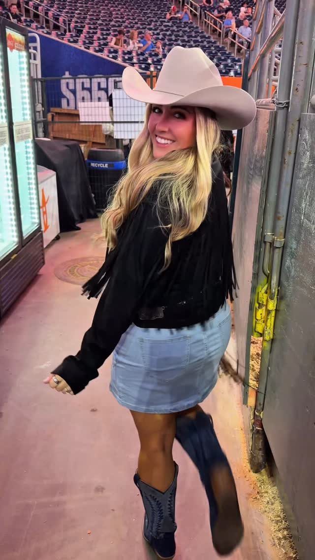 Woman in cowboy hat and denim skirt wearing dark blue western boots.