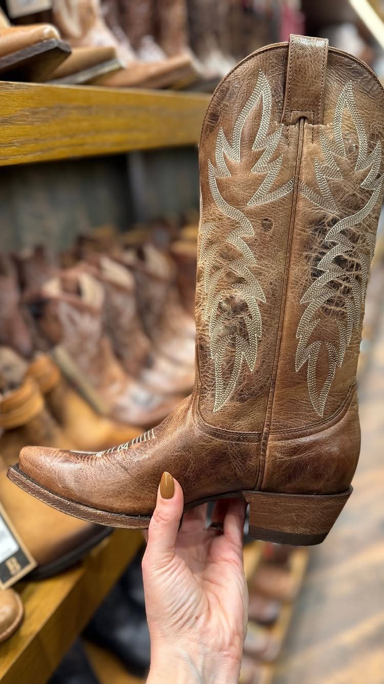 Tan leather western boot with decorative stitching and snip toe held by hand