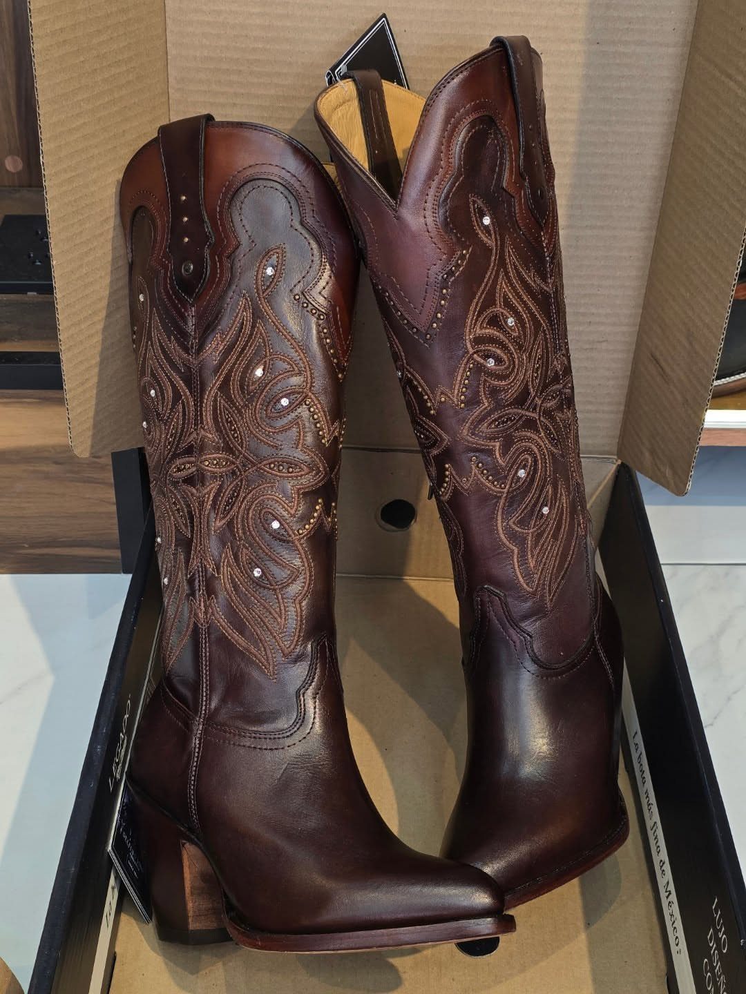 Brown leather western cowgirl boots with decorative stitching inside a cardboard box