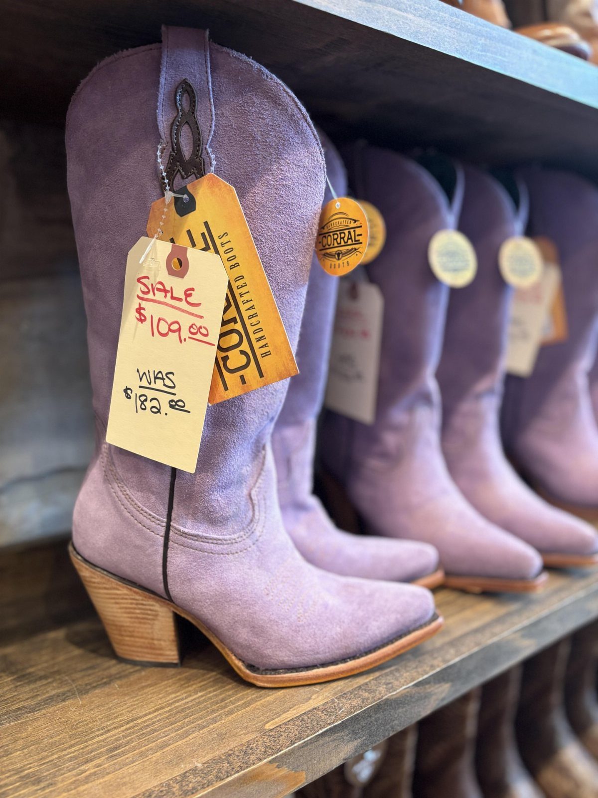 Light purple suede cowgirl boots with wooden heels on a store shelf