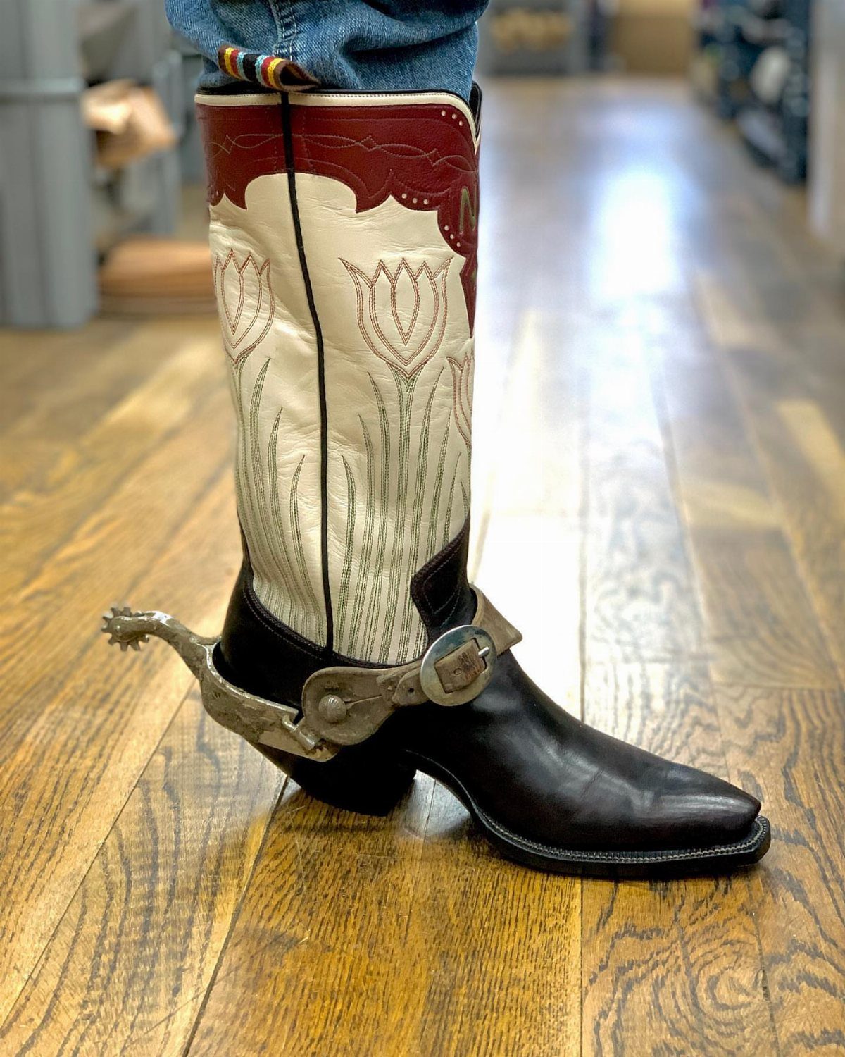Pointed toe western boot with white floral shaft and silver spur on wooden floor