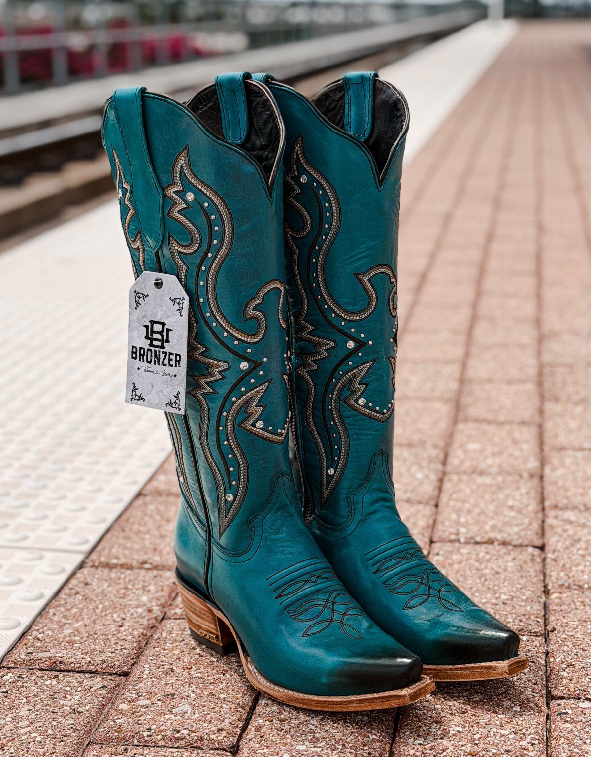 Turquoise leather western boots with gold embroidery standing on a red brick walkway.