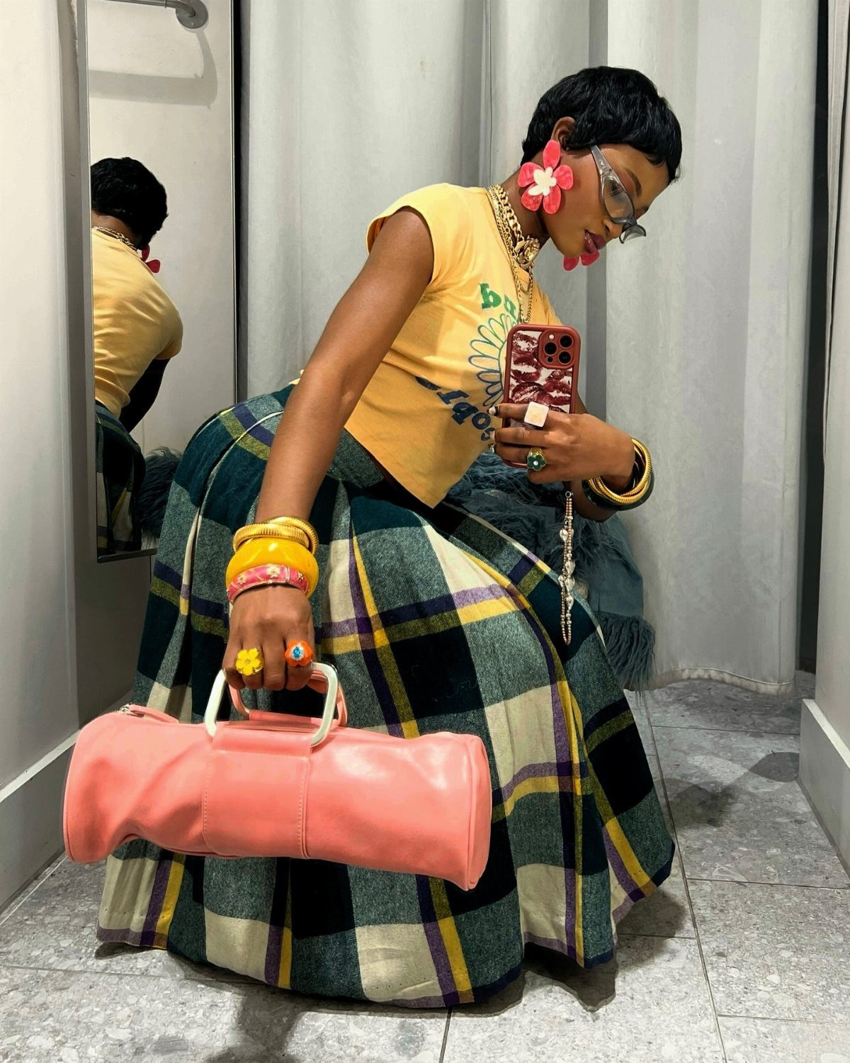 Woman in yellow t-shirt and plaid skirt posing with a pink handbag.