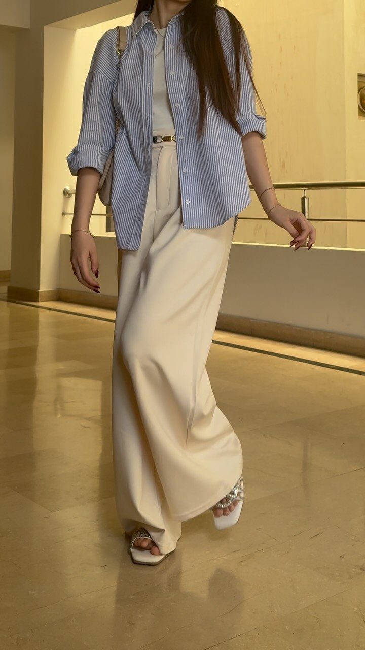 Woman wearing a striped blue shirt and cream maxi skirt in a hallway