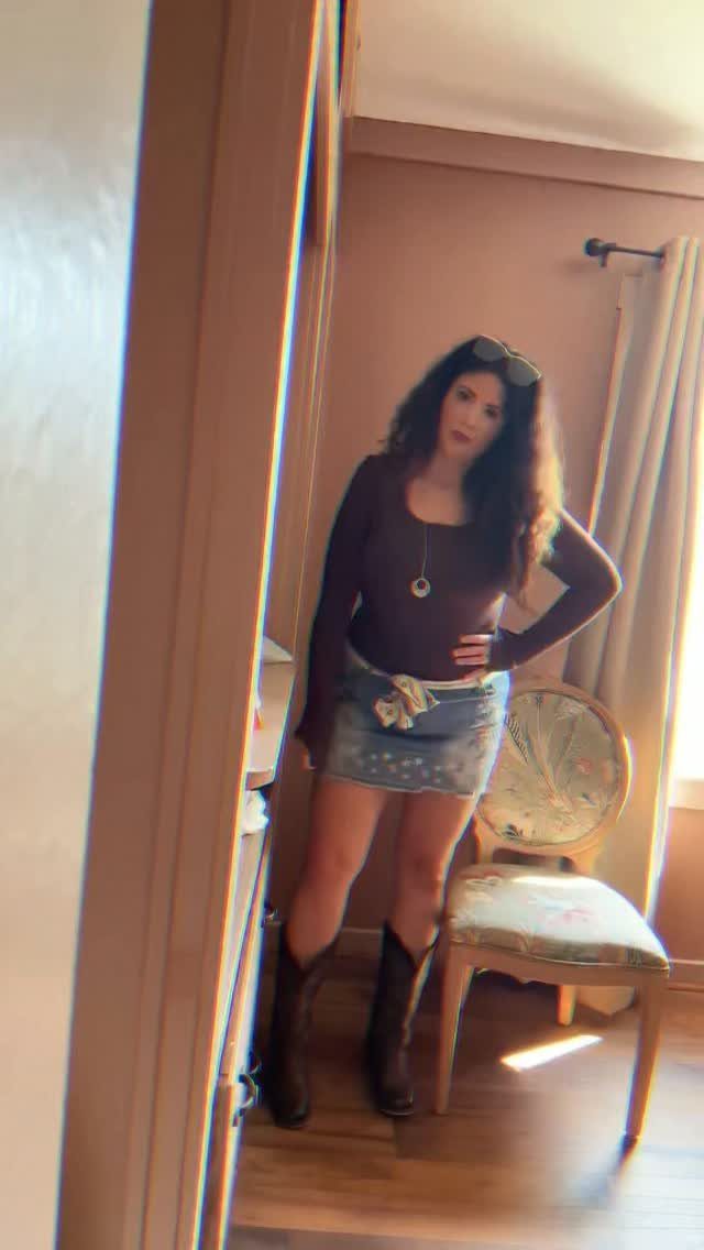 Woman wearing a purple top, denim mini skirt, and black knee-high boots.
