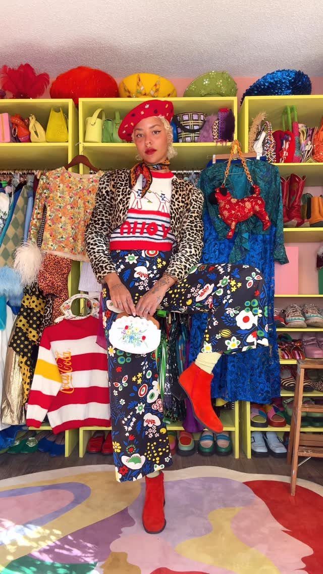 Woman in eclectic colorful outfit posing in a room full of vibrant clothing.