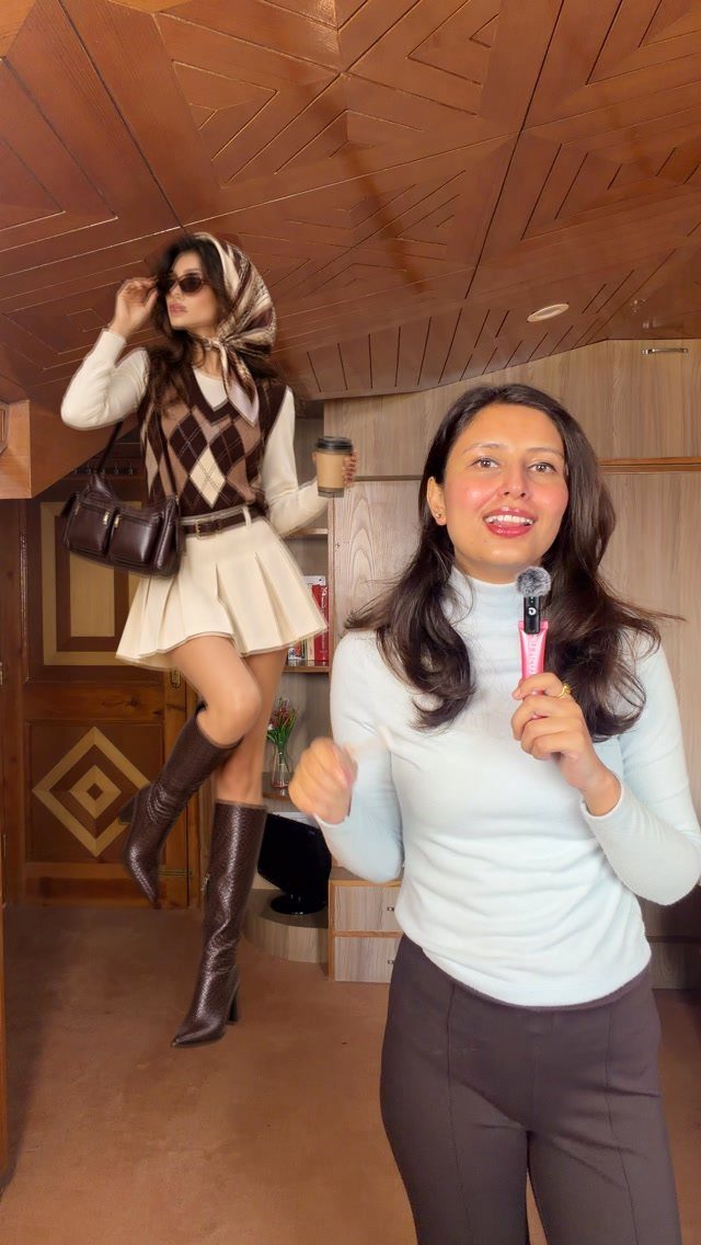 Woman in argyle vest and pleated skirt posing behind a woman with a microphone.