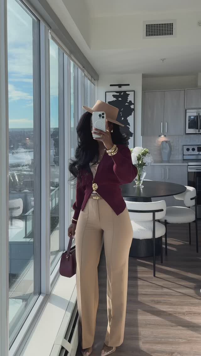 Woman in burgundy blazer and tan trousers posing for a mirror selfie indoors.