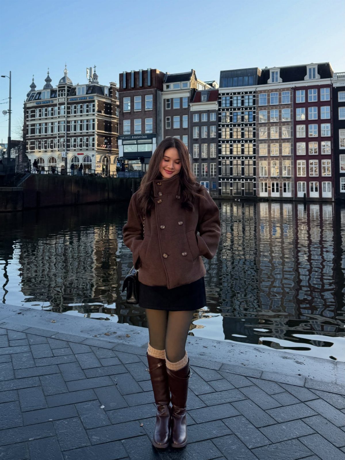 9 Dress and Coat Outfit Ideas for Work, Evenings and More 2 Woman wearing a brown peacoat and black dress standing by a city canal.