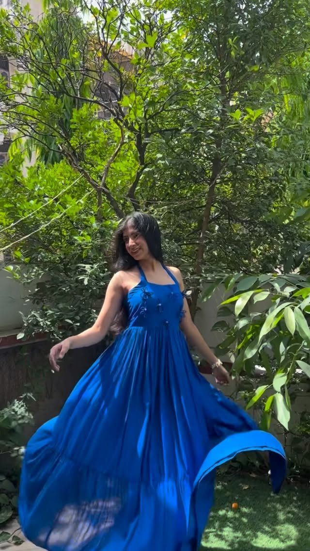 Woman in a royal blue halter neck maxi dress standing in a green garden