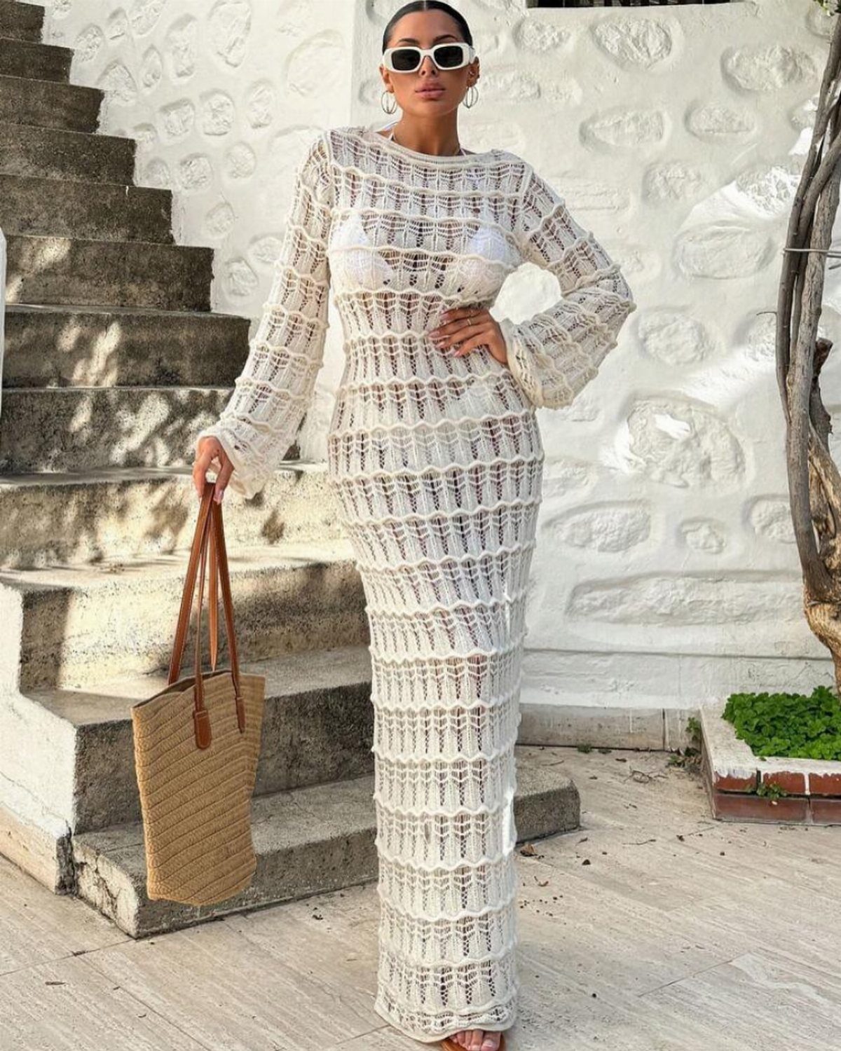 Woman in a white crochet cover-up dress and straw bag by stone stairs