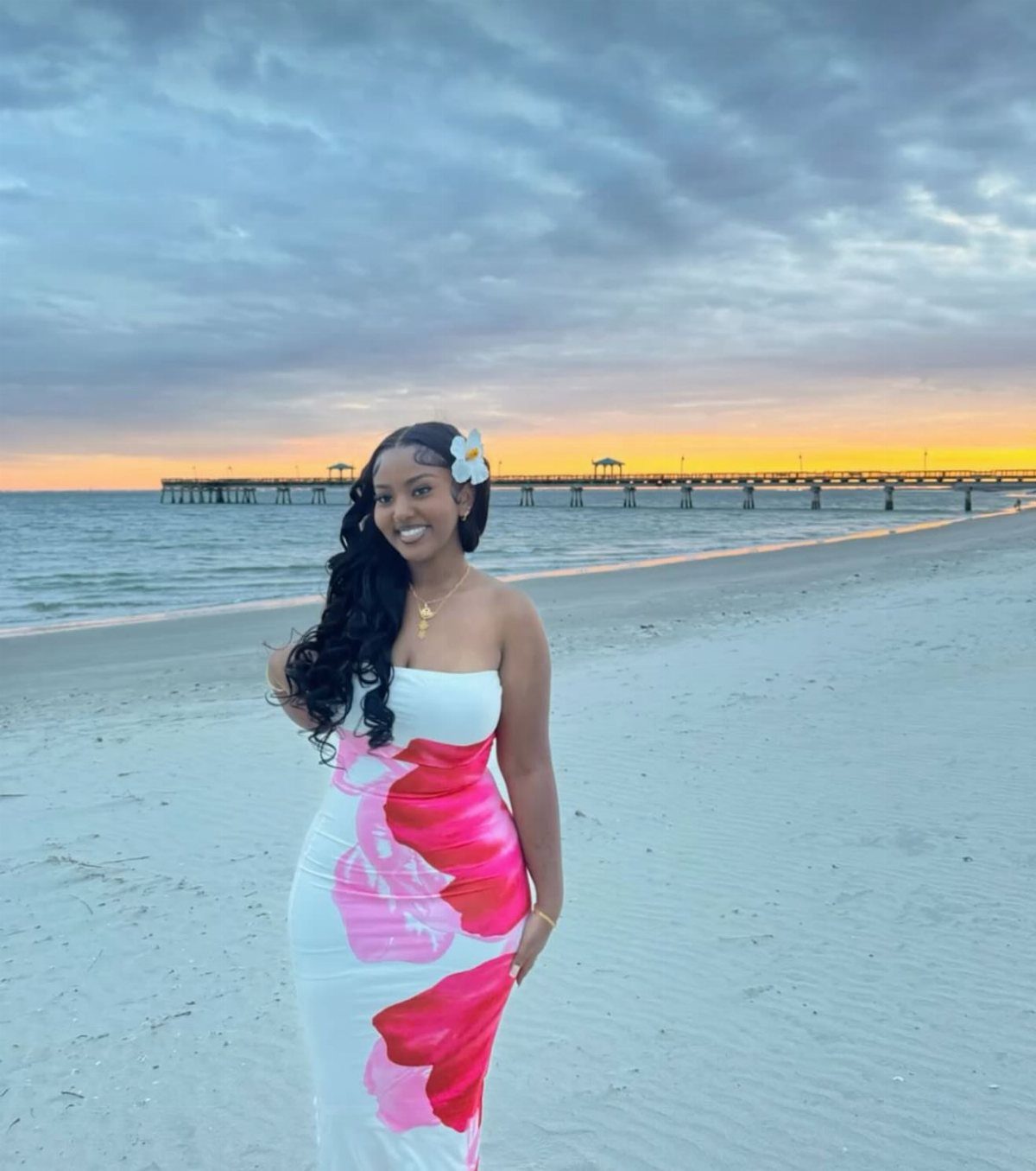 Woman in a white strapless maxi dress with pink floral print on a beach