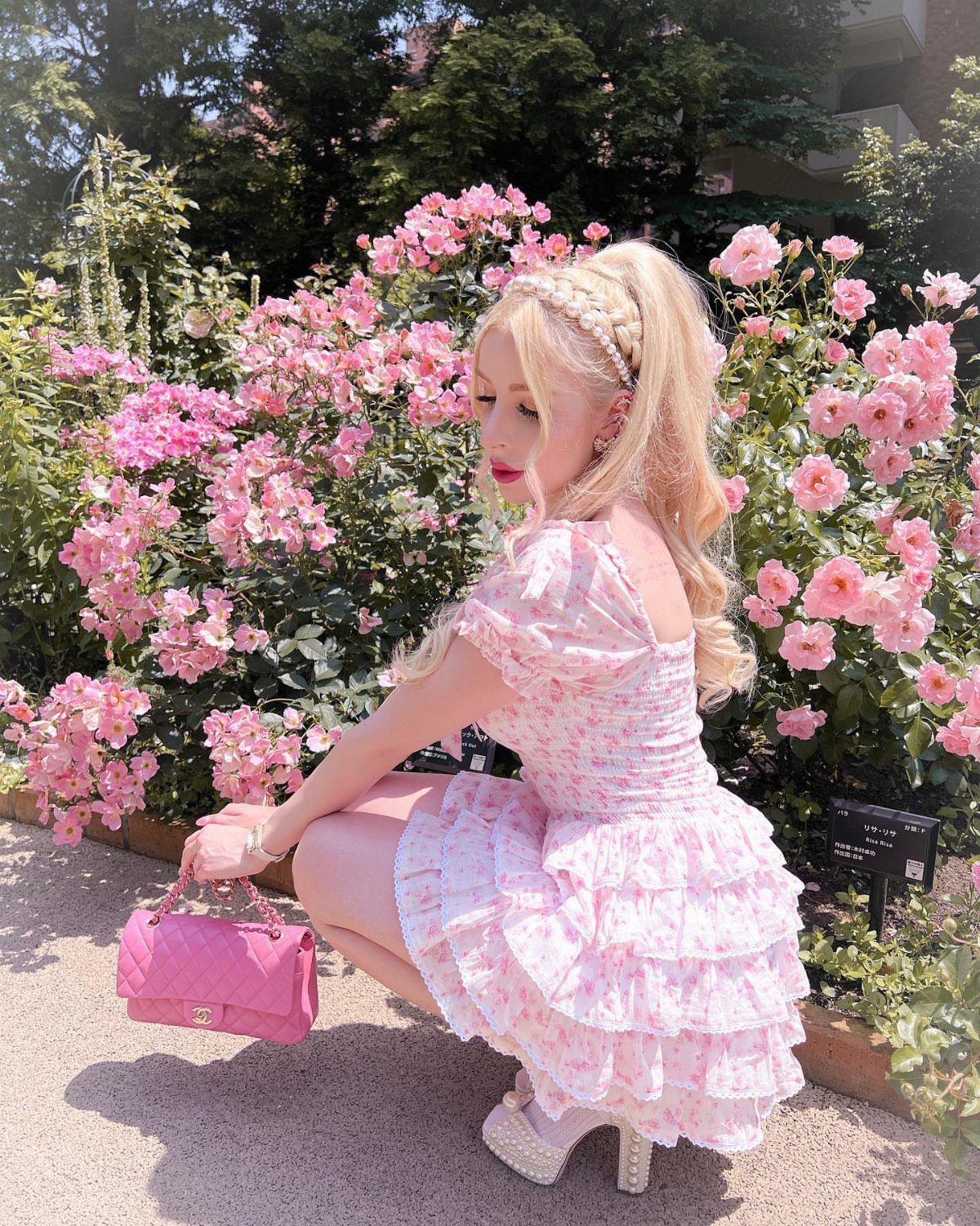 Woman in a pink floral tiered dress posing among blooming pink roses.