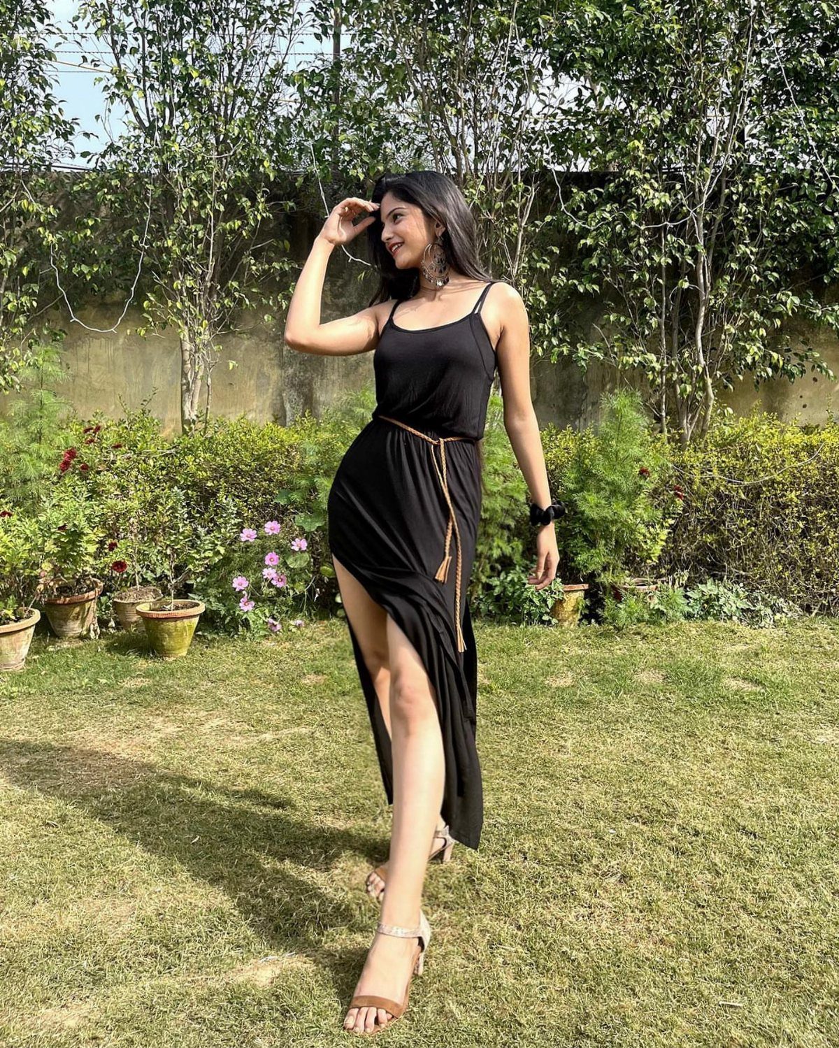 Woman in a black sleeveless midi dress with a slit and brown belt.