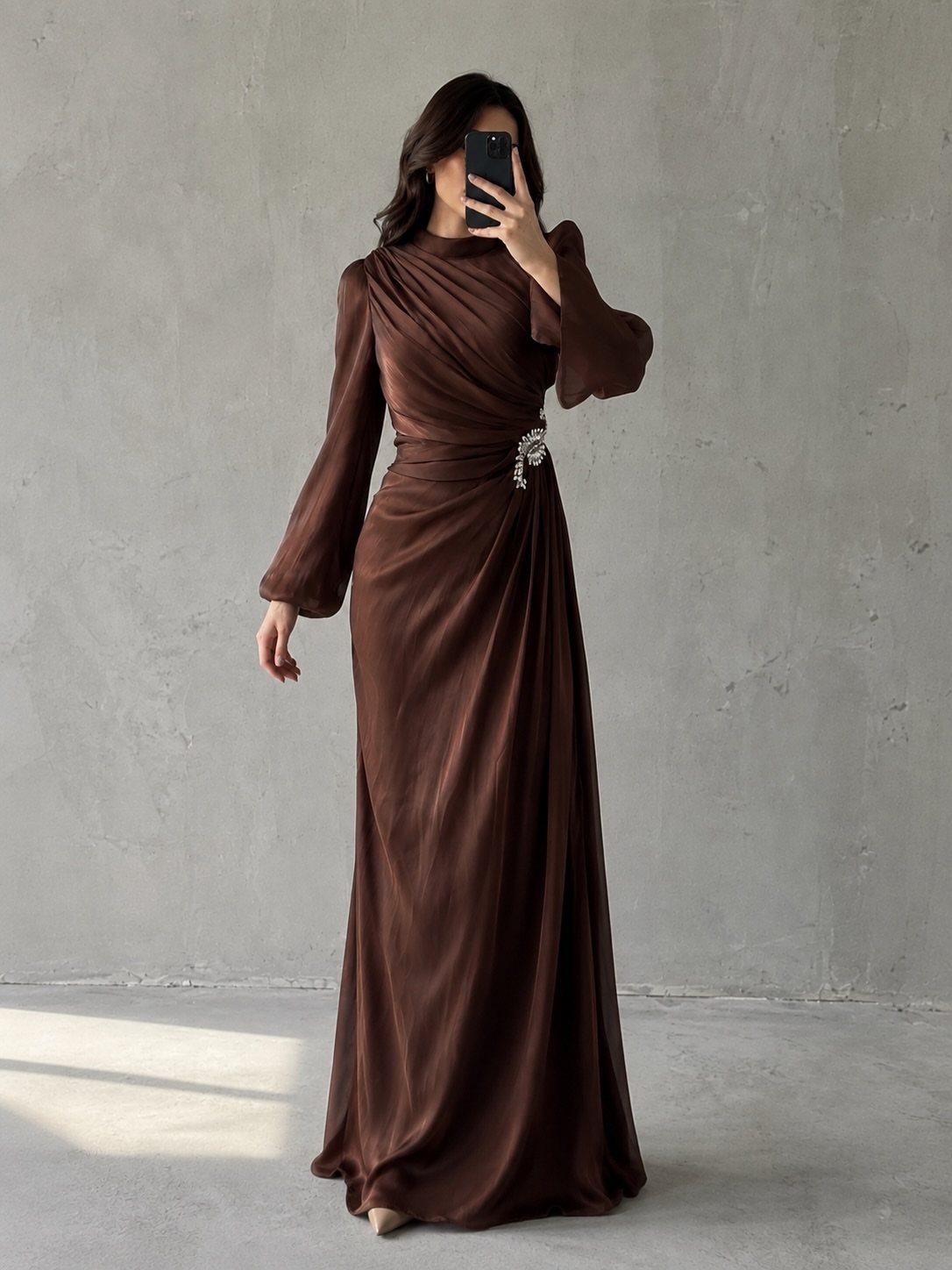 Woman in a long-sleeved brown satin maxi dress with a jeweled waist detail.