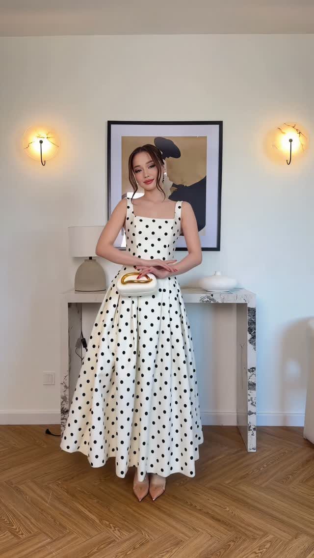 Woman wearing a white midi dress with black polka dots and a white handbag.
