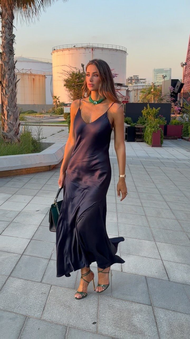 Woman in a navy blue satin slip dress and green heels on a walkway.