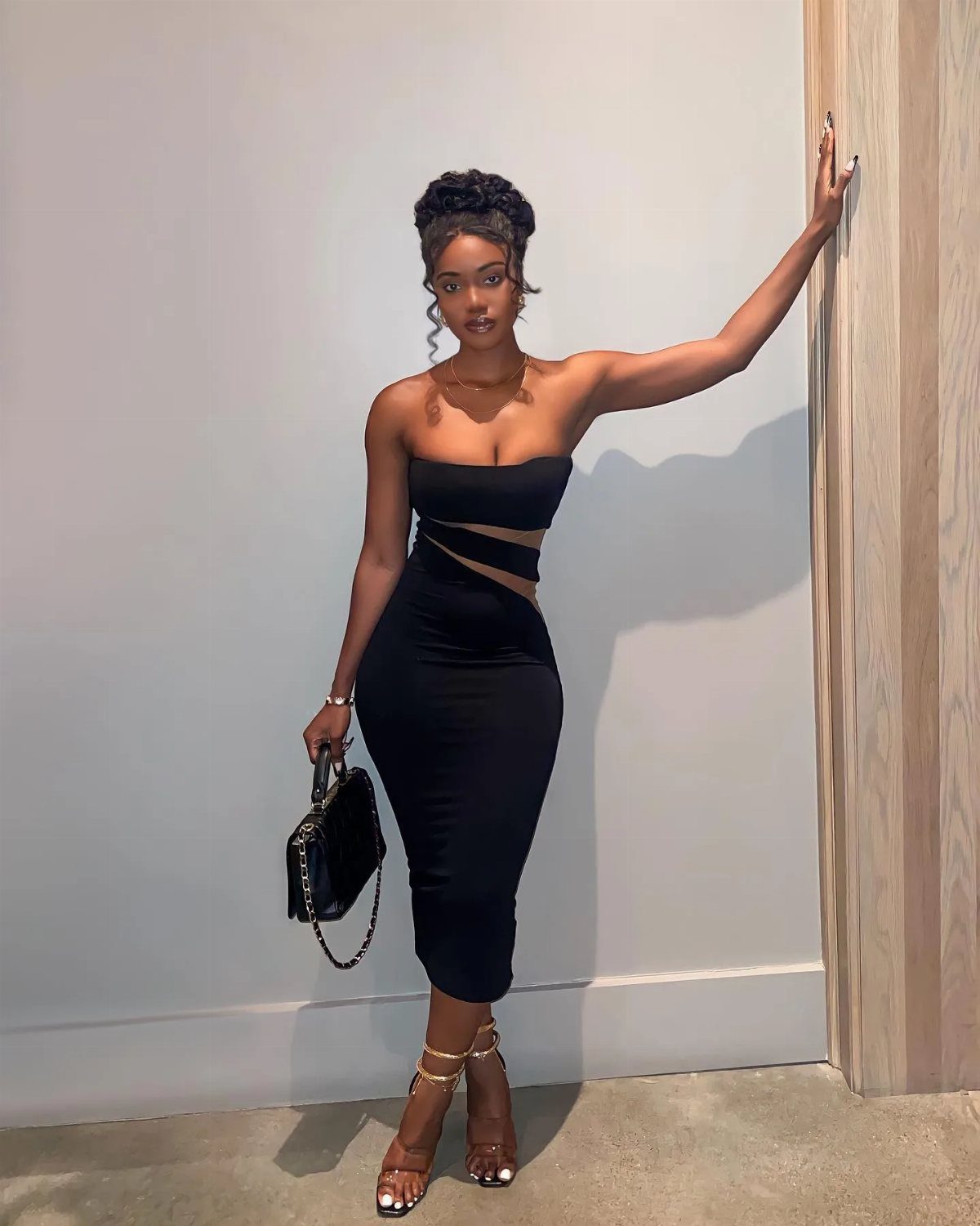 Woman wearing a strapless black midi dress with sheer cut-outs and gold heels.